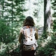 girl with brown hair walking through the woods with a backpack on